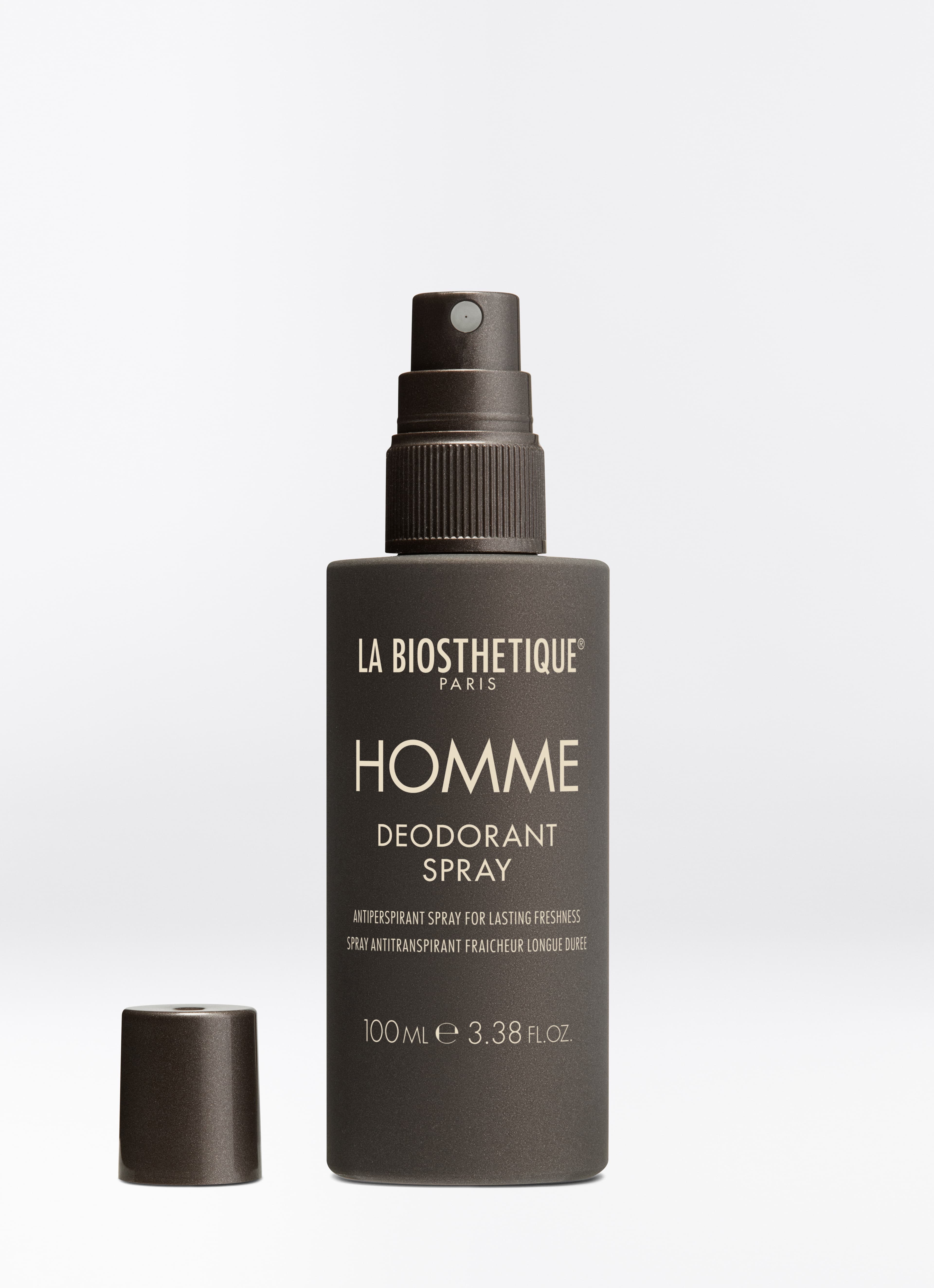 Dunkelbraune Sprühflasche des Homme Deodorant Sprays mit abgenommener Kappe auf hellgrauem Hintergrund.