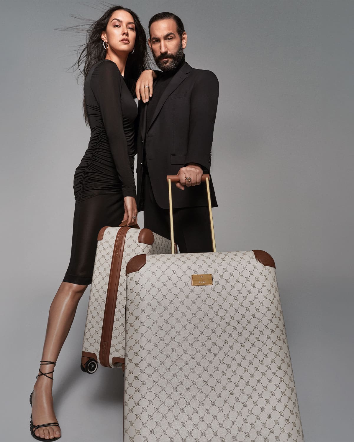 JOOP! luggage a man and woman both dressed in black carrying a suitcase in beige with cornflower pattern and brown corners