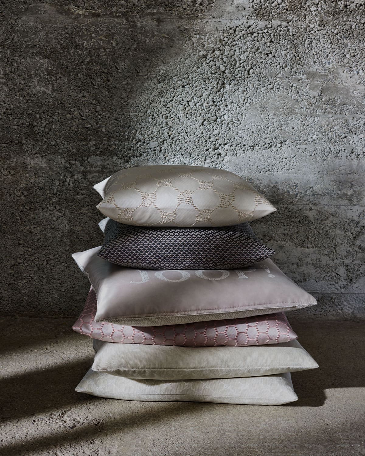 JOOP! living various cushions stacked on a concrete floor and in front of a concrete wall