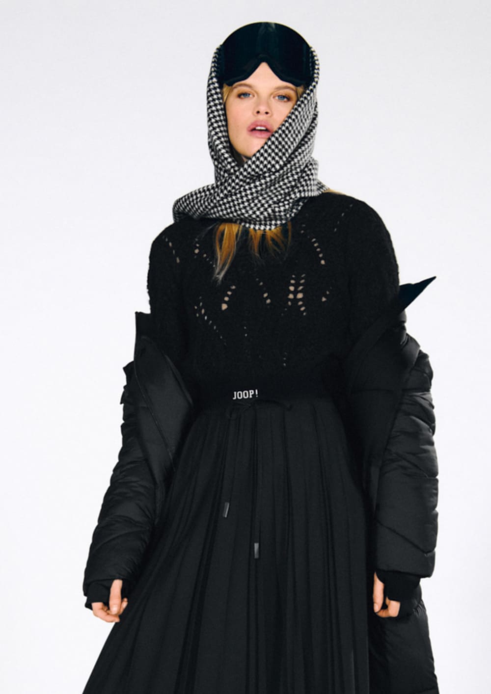 Woman in a black Joop knit sweater with a black coat and a black pleated skirt
