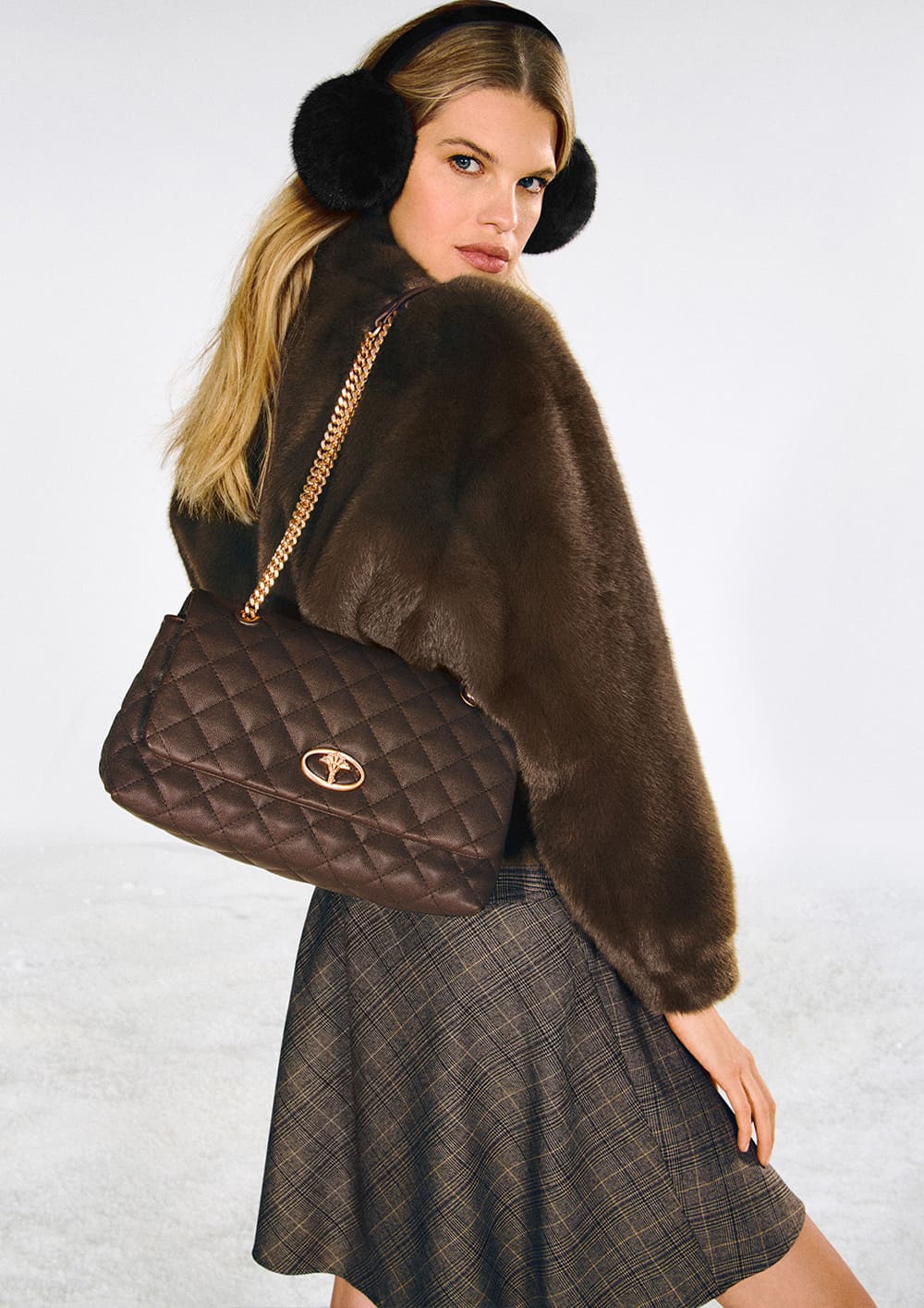 Woman wearing a brown Joop faux fur short jacket with a brown plaid skirt and a brown quilted bag