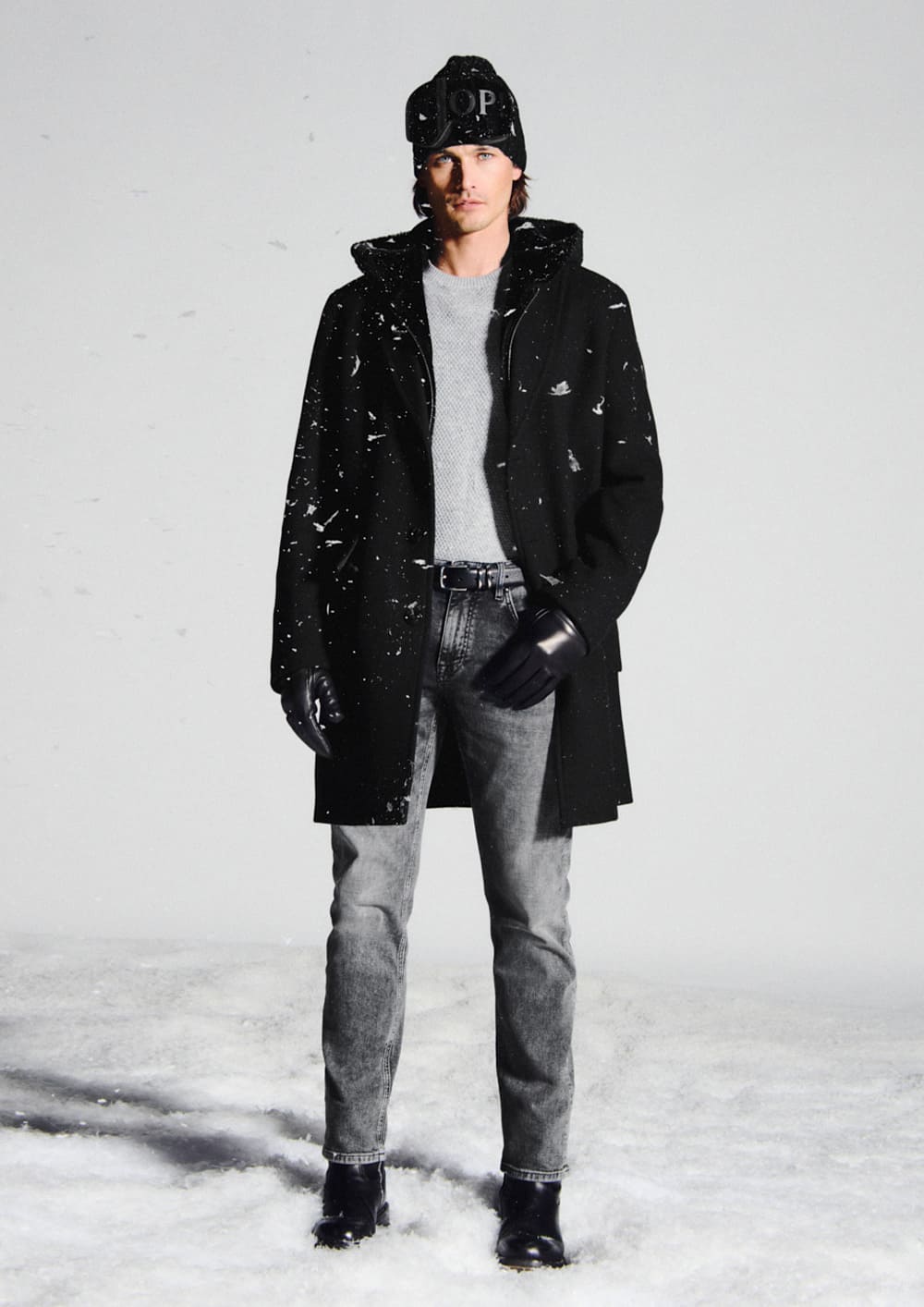 Joop, a man wearing a light gray sweater, a black coat, and gray jeans