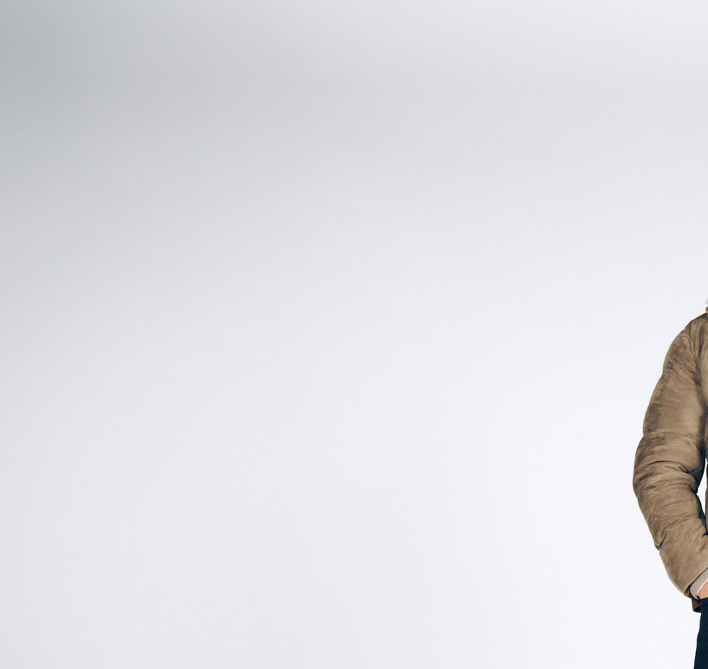 Joop, a man wearing a brown lined jacket, a cream-colored turtleneck sweater, and jeans