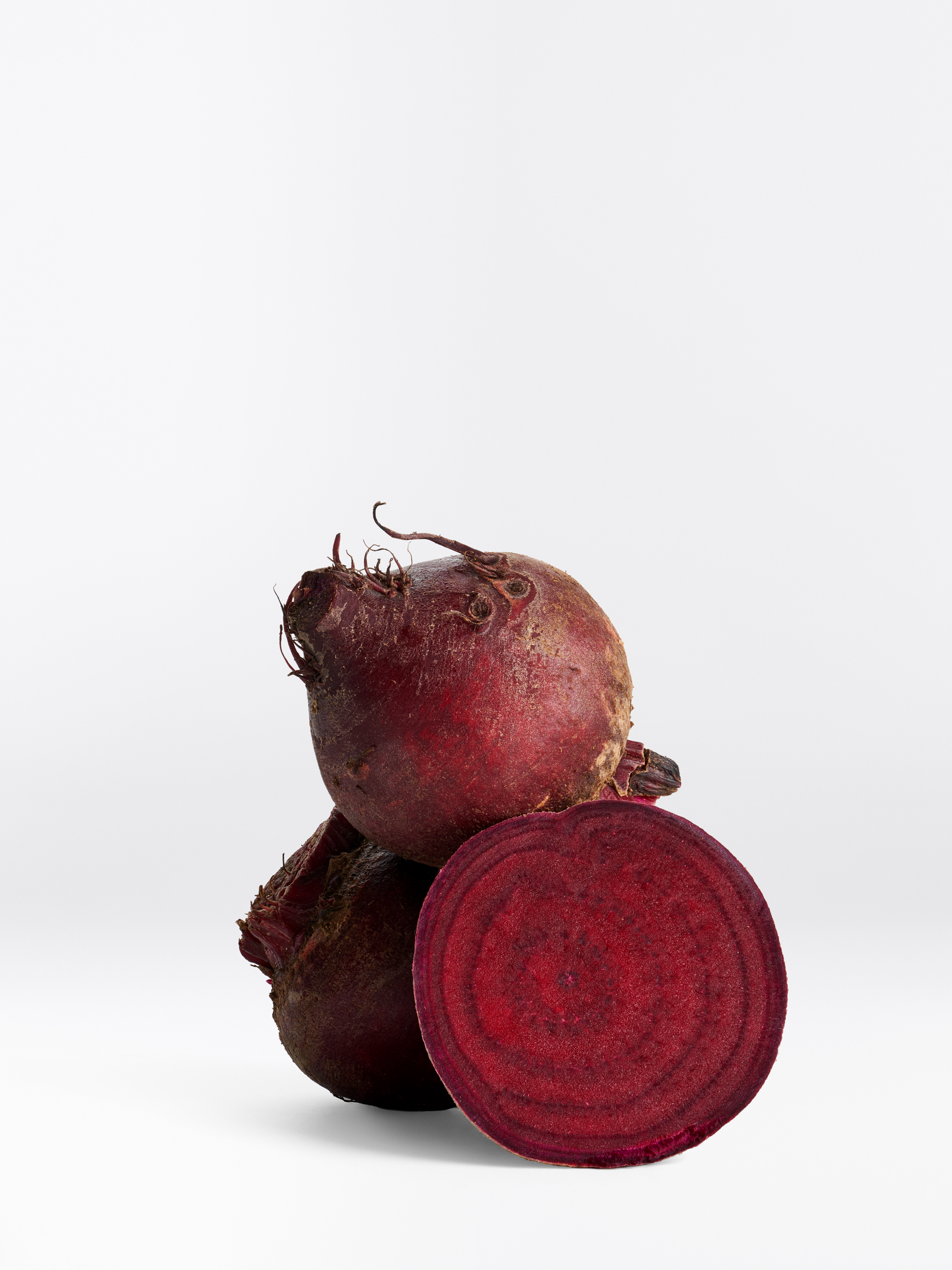 Zwei ganze runde Rote Bete Knollen und eine Hälfte einer aufgeschnittenen Rote Bete Knolle.