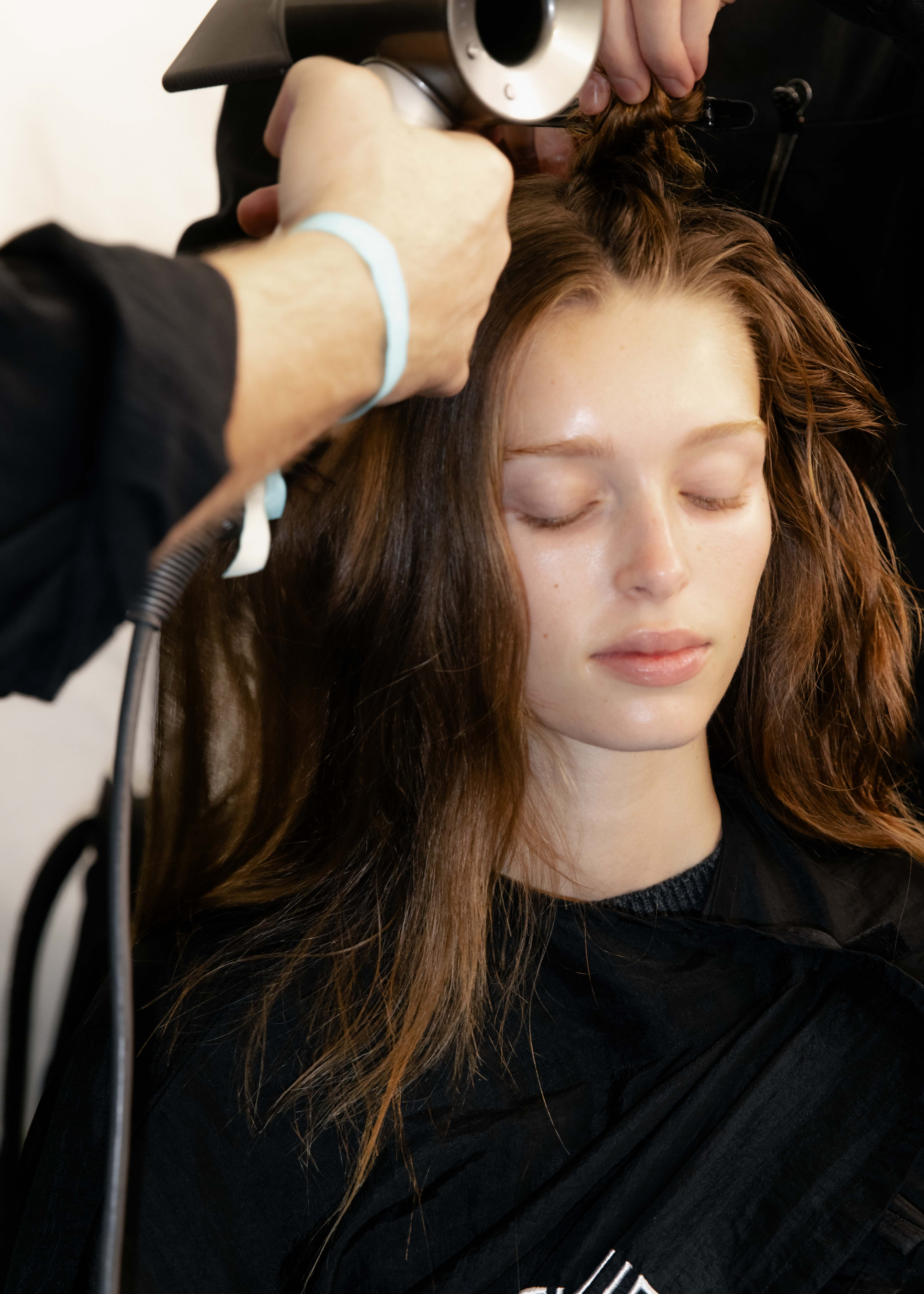 Frau mit schulterlangen braunen Haaren bekommt die Haare geföhnt. 