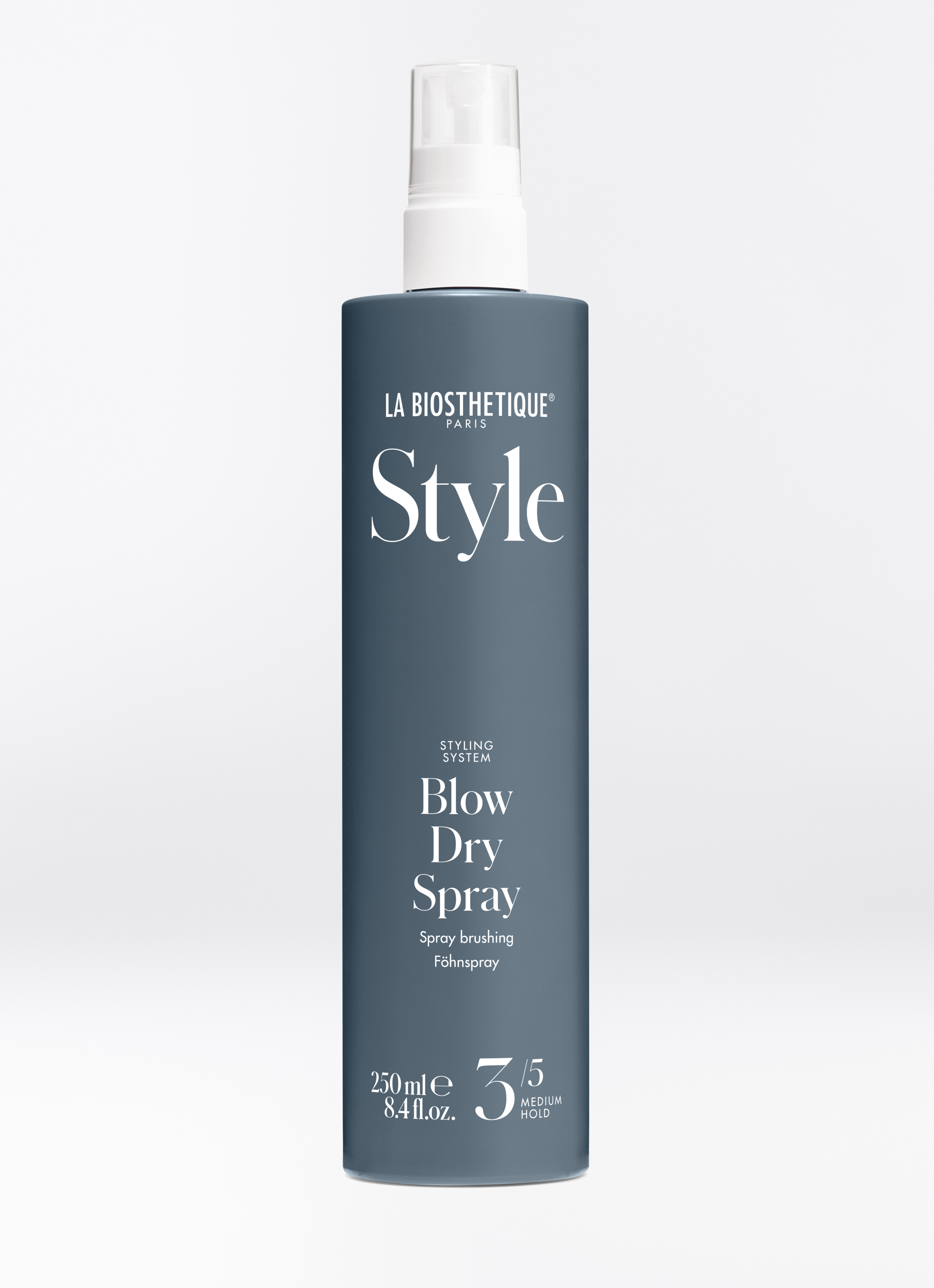 Dunkle, stahlblaue Sprühflasche des Blow Dry Spray auf hellgrauem Hintergrund.